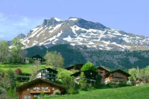 A mountain with snow on top and houses in the background.